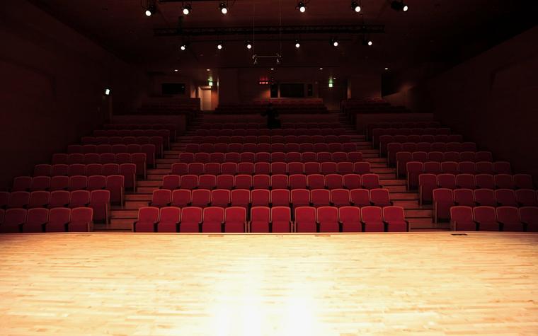 Een lege schouwburg met rode stoelen en een verlicht podium, sfeerbeeld bij de Aurora demo