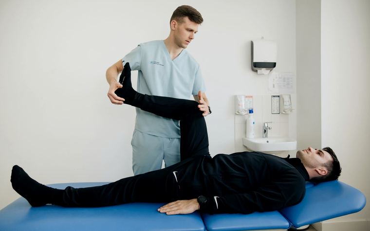Een kinesitherapeut die het been van een patient strekt op de behandeltafel